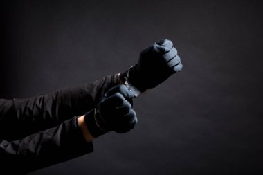 Siyah eldivenli, siyah arka planda kelepçeli bir hırsızın elleri.