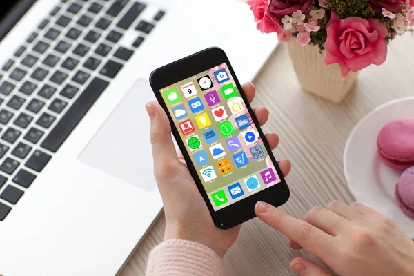 Women hands holding phone with home screen icons apps laptop — Stock Photo, Image