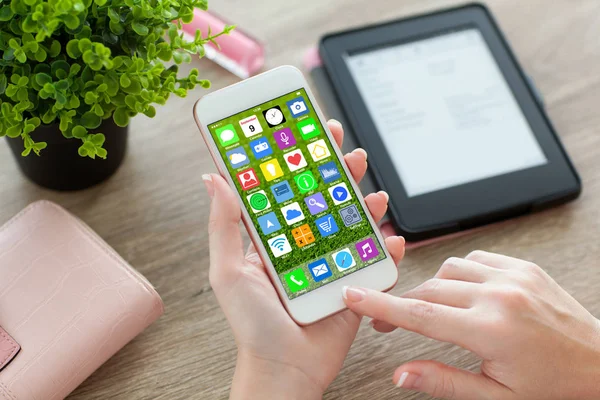 Female hands holding white phone with home screen icons apps — Stock Photo, Image