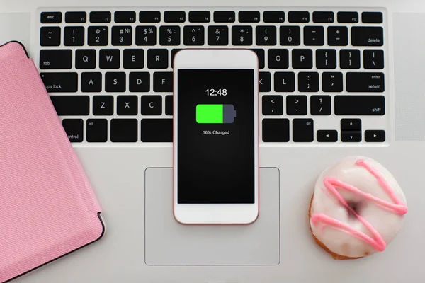 Teléfono rosa blanco con pantalla de batería cargada en teclado portátil —  Fotos de Stock