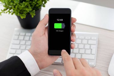 adam telefon şarj edilmiş bir batarya ile ekran üzerinde tutarak ofis