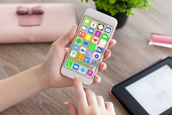 Female hands holding white phone with home screen icons apps — Stock Photo, Image