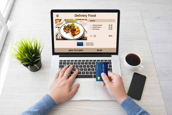 Mãos de homem segurando cartão de crédito e laptop com entrega de alimentos — Fotografia de Stock