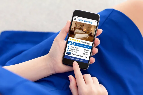 Γυναίκα με μπλε φόρεμα κρατώντας το τηλέφωνο με το app κράτησης ξενοδοχείου — Φωτογραφία Αρχείου