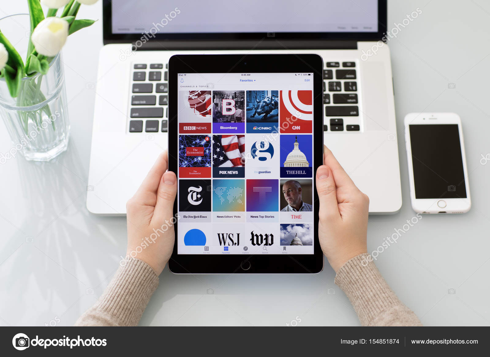 Tangan wanita memegang iPad Pro dengan aplikasi berita populer