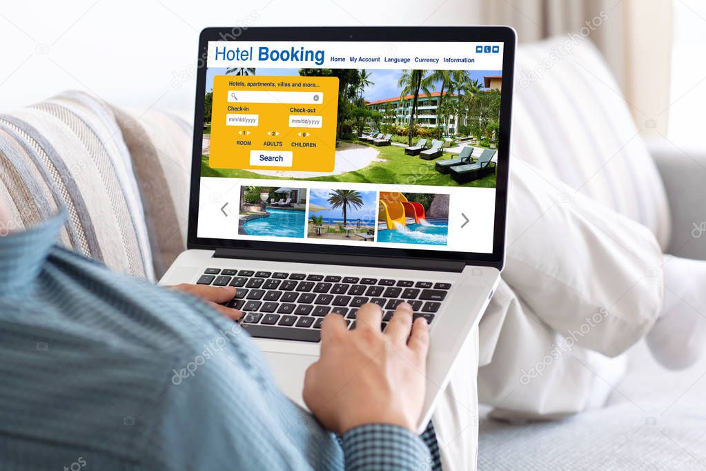 man in room holding laptop with online search booking hotel