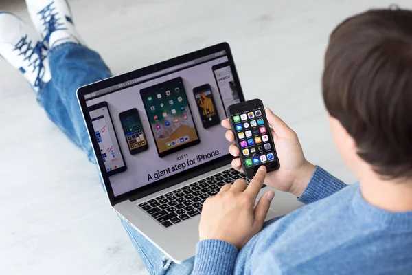 Hombre de la mano iPhone con IOS en la pantalla y MacBook —  Fotos de Stock