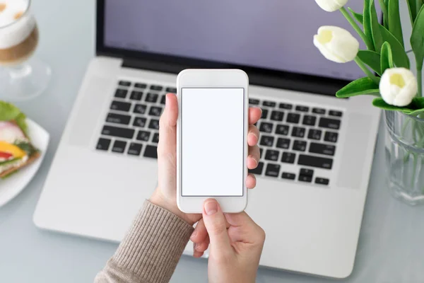 Frauenhände halten Telefon mit isoliertem Bildschirm in der Nähe von Laptop — Stockfoto