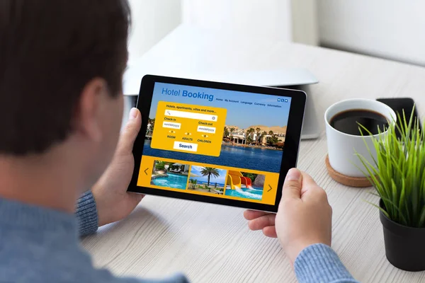 Uomo in ufficio in possesso di tablet computer con prenotazione app hotel — Foto Stock