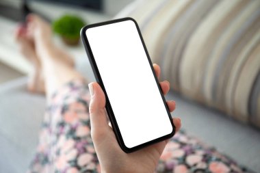 Kadın elleri kanepeye uzanmış telefonu tek bir ekran ile tutuyor.