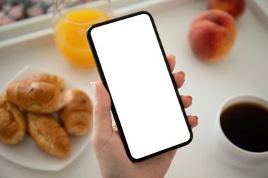 Kadın eli telefonu kahvaltı masasında tek başına tutuyor.