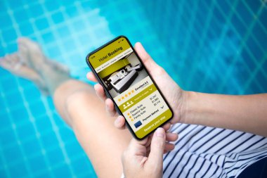 Havuzdaki ekranda uygulamalı otel rezervasyonu olan kadın elleri.