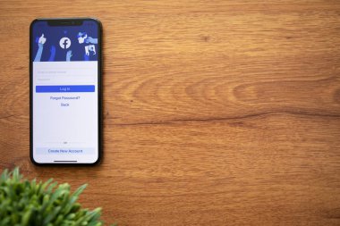 Anapa, Russia - August 1, 2019: iPhone X with social networking service Facebook on the screen and background wooden desk. iPhone was created and developed by the Apple inc.