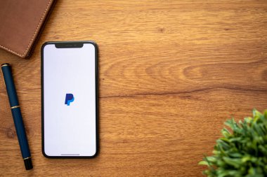 Anapa, Russia - August 1, 2019: iPhone X with service PayPal on the screen and background wooden desk. iPhone was created and developed by the Apple inc.