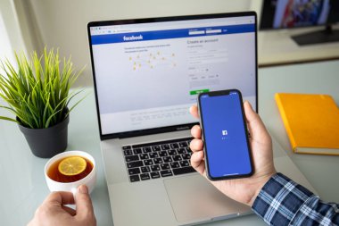 Anapa, Rusya - 22 Şubat 2020: Man hand holding iPhone 11 on Macbook Pro 16 üzerinde sosyal ağ hizmeti Facebook ekranında. Macbook ve iPhone Apple tarafından yaratıldı ve geliştirildi..