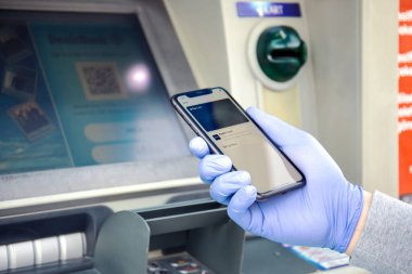 Alanya, Türkiye - 24 Mart 2020: ATM ekranında Apple Pay Cash ile birlikte iPhone 11 'i tutan tek kullanımlık koruyucu eldiven.