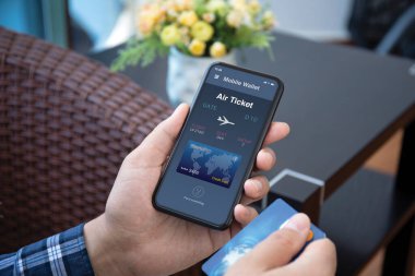 Erkek eli, ekranda uçak bileti başvurusu yapan havayolu şirketinin telefonuyla odadaki kredi kartını tutuyor.