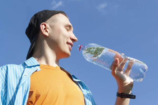 Guy drinking water from a bottle against a blue sky — Stock Photo, Image