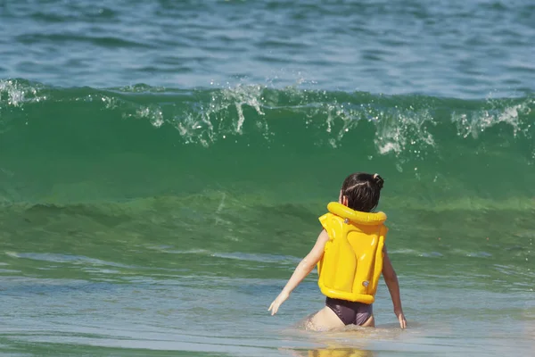 Маленька дівчинка в жовтій куртці стоїть перед великою хвилею — стокове фото