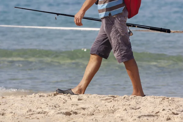 Um pescador caminha ao longo da praia com uma vara de pesca na mão — Fotografia de Stock