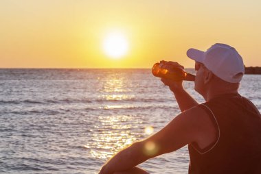 Bira içen bir adam deniz batımında arka planda