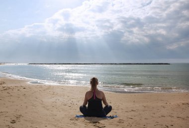 Kız güneşin altında sahilde meditasyon yapıyor.