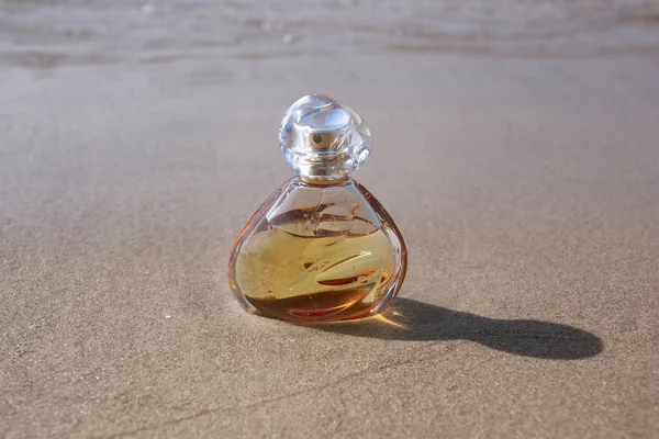 Frasco de perfume na areia contra a água do mar — Fotografia de Stock