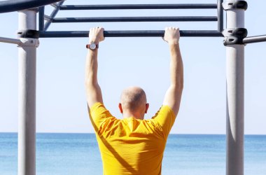 Sahildeki spor sahasında yatay bardaki adam.