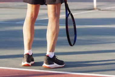 The legs of an elderly man standing with a racket on the court clipart