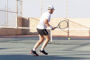 Yaşlı bir adam dışarıda tenis oynuyor.
