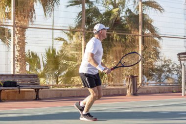 Yaşlı bir adam dışarıda tenis oynuyor.