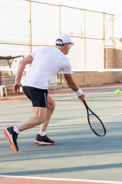 Yaşlı bir adam dışarıda tenis oynuyor.