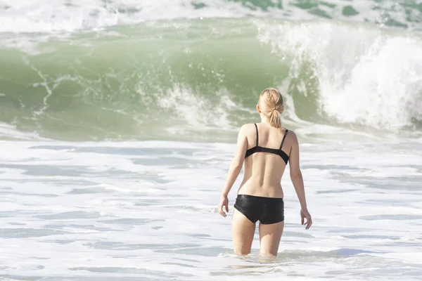 A fragile girl standing in front of an approaching wave — 스톡 사진