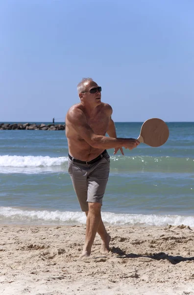 Schöner erwachsener Mann spielt Tennis am Strand — Stockfoto