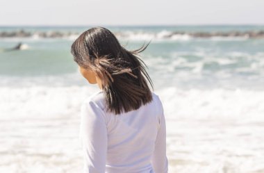 Saçları rüzgarda dalgalanan genç bir kız denize karşı