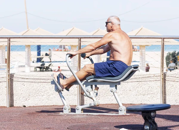 Hombre adulto haciendo ejercicios en un simulador de deportes en el campo de deportes — Foto de Stock