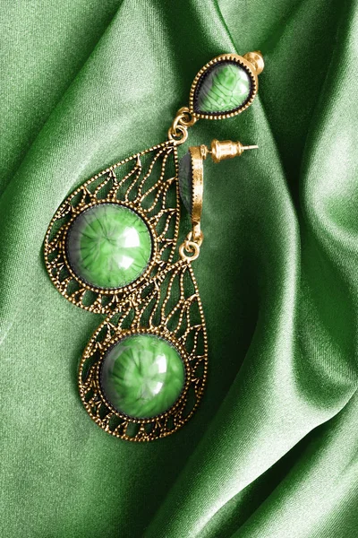 Earrings on green satin — Stok fotoğraf