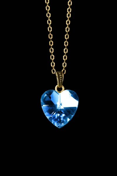 蓝色水晶心形吊坠挂在黑色背景的金链上 免版税图库照片