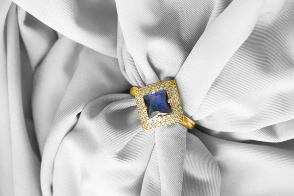 Gold sapphire ring with diamonds on white draped silk