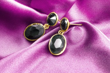 Mor pembe saten arka planda siyah akik altın küpeler.