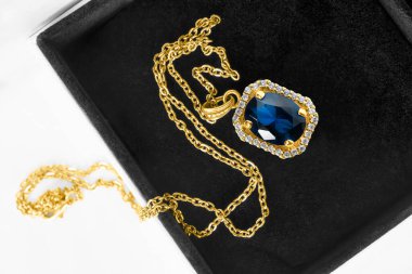 Siyah mücevher kutusunda safir kolyesi olan güzel altın bir kolye.