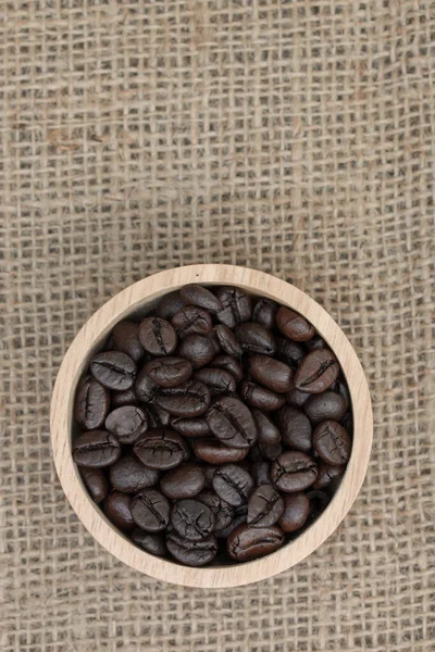 Vista dall'alto: Chicchi di caffè in tazza di legno su sfondo texture sacco — Foto Stock