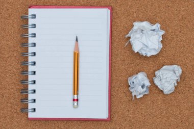 Mantar kaplama arka planında buruşmuş kağıt top olan defter ve kalemi aç.