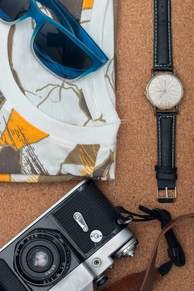 Vista superior de la ropa y accesorios: camisa, gafas de sol, reloj de pulsera y cámara en el suelo de madera . — Foto de Stock