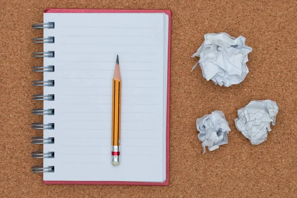 Caderno aberto e lápis com bola de papel amassada no fundo da placa de cortiça . — Fotografia de Stock
