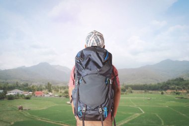 Sırt çantalı genç adam pirinç tarlasına ve köye bakıyor..