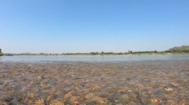 Çakıl taşları ve taşlarla akan su akıntısı dağ manzaralı bir nehir boyunca ve mavi gökyüzü arka planında.