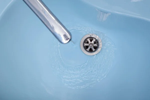 Вода течет из крана в синей раковине — стоковое фото