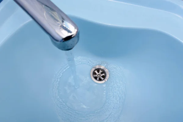 Water flows from the tap in a blue washbasin — Stock Photo, Image