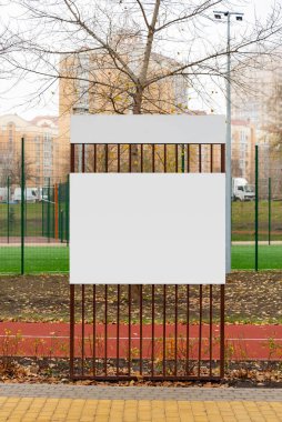 Sonbaharda parkta boş beyaz bilgi panosu. Çıplak ağaçlar ve yerde sonbahar yaprakları.